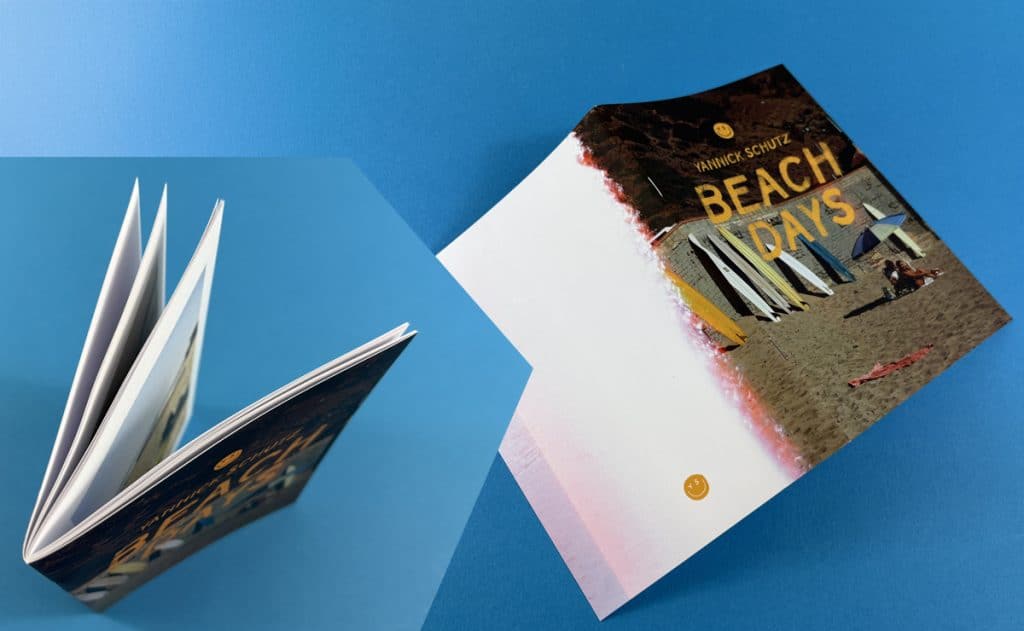 Open saddle-stitched booklet and printed cover booklet on blue background, showing flat-opening booklet binding.