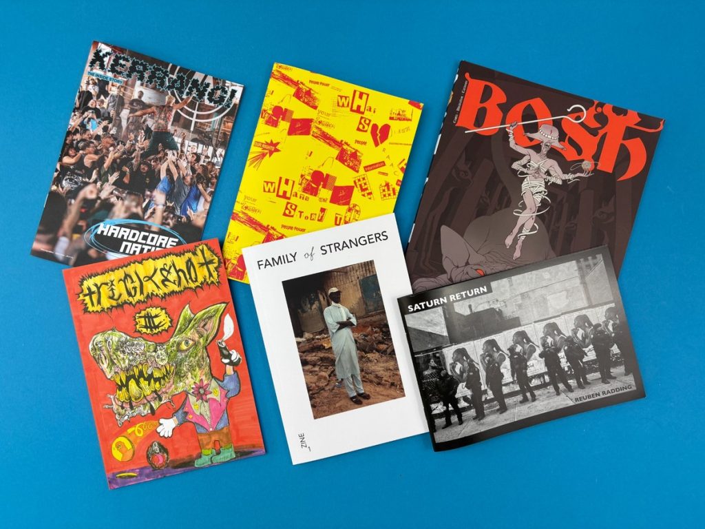 A selection of printed zines on a blue background illustrating the range of styles covered in this guide to the best zine printing companies in the UK.