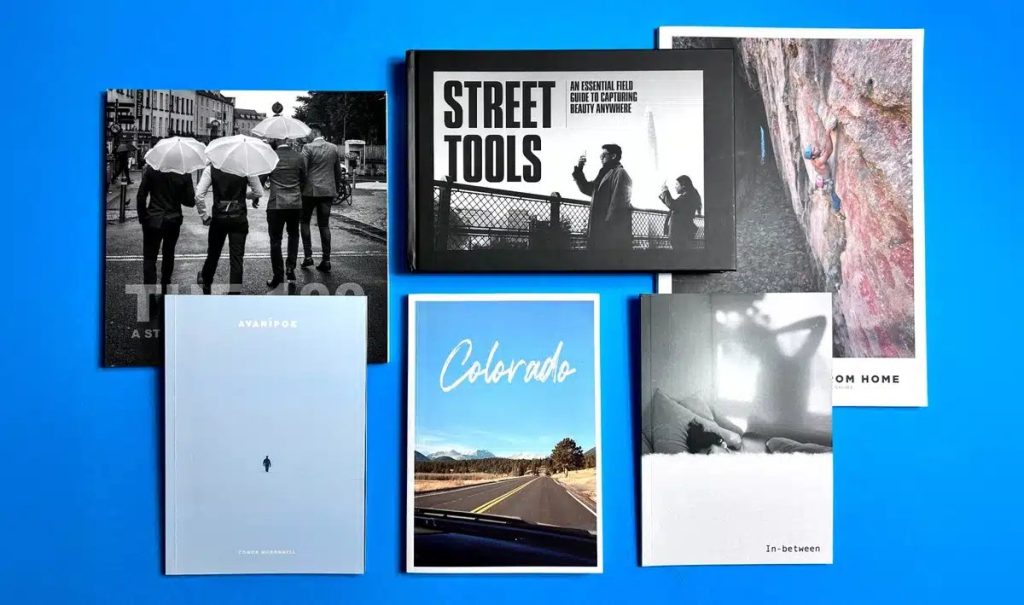 Selection of Ex Why Zed photobooks on a blue backdrop, illustrating glossy vs matte print finishes for photography.