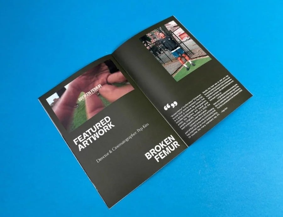 Open printed magazine spread on a blue table showing featured artwork and a bold black editorial layout.