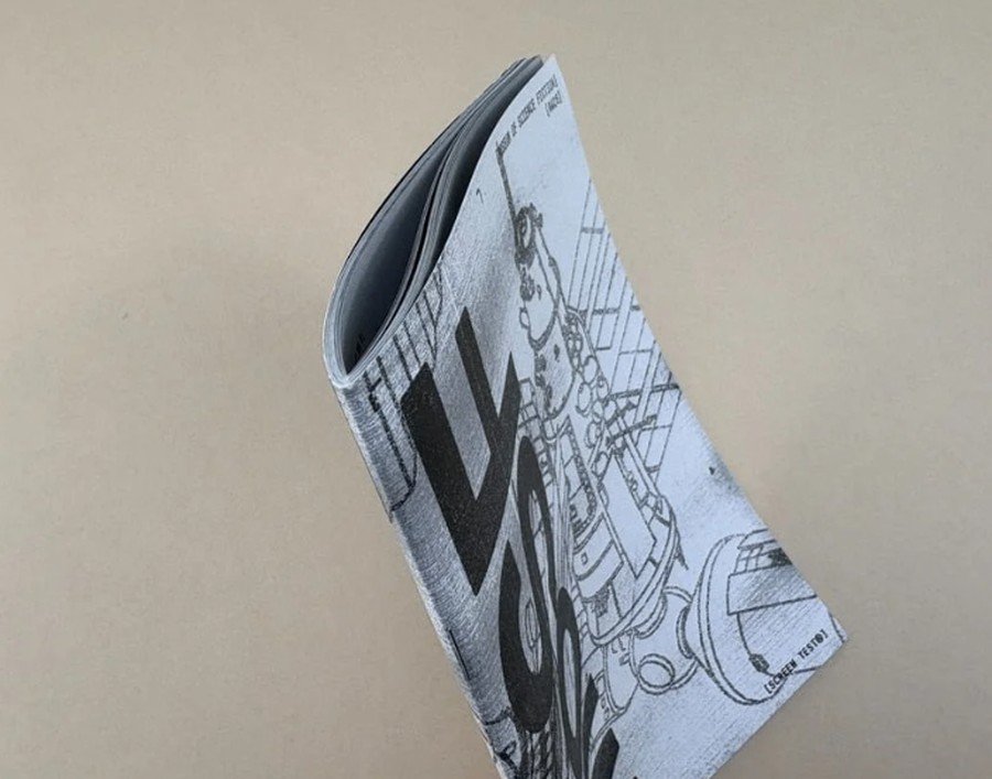 Stapled black and white zine standing upright, used to compare online and local magazine printing options.