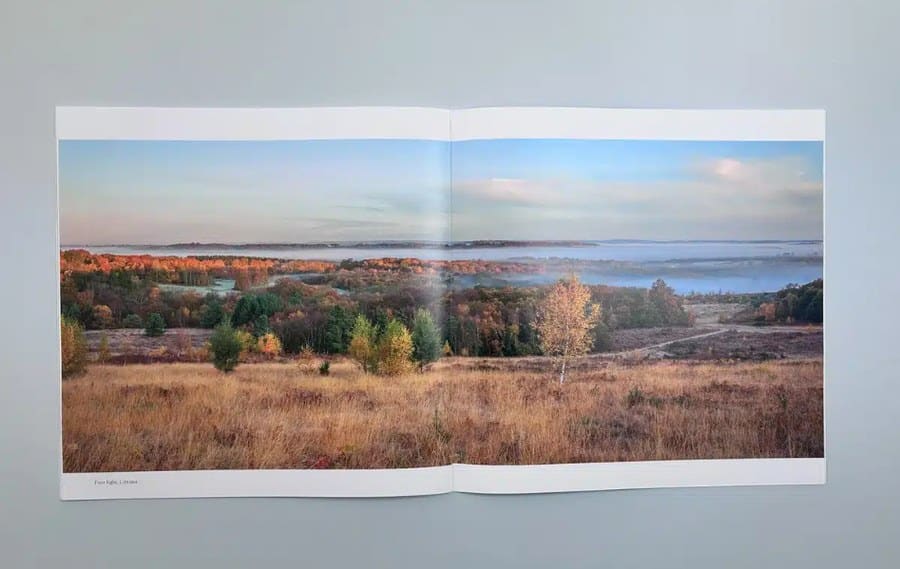 A full-bleed landscape photograph running across a printed booklet spread, showing why 3mm bleed is needed for edge-to-edge designs
