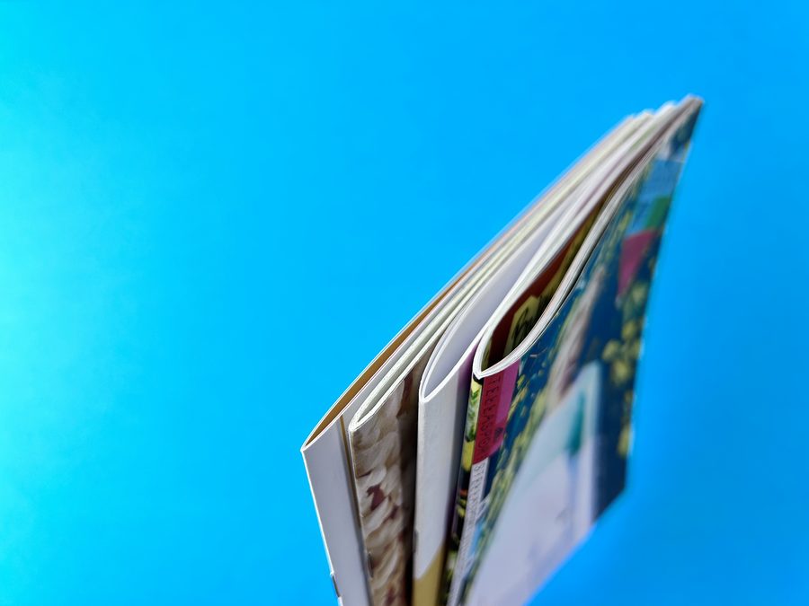 Top-down view of stapled booklets: a slim booklet sits flat while a thicker one springs open at the centre.