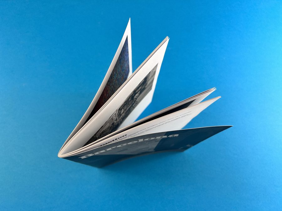 A wire stitched booklet stood upright with its pages fanning open, showing the centre curl known as bounce.
