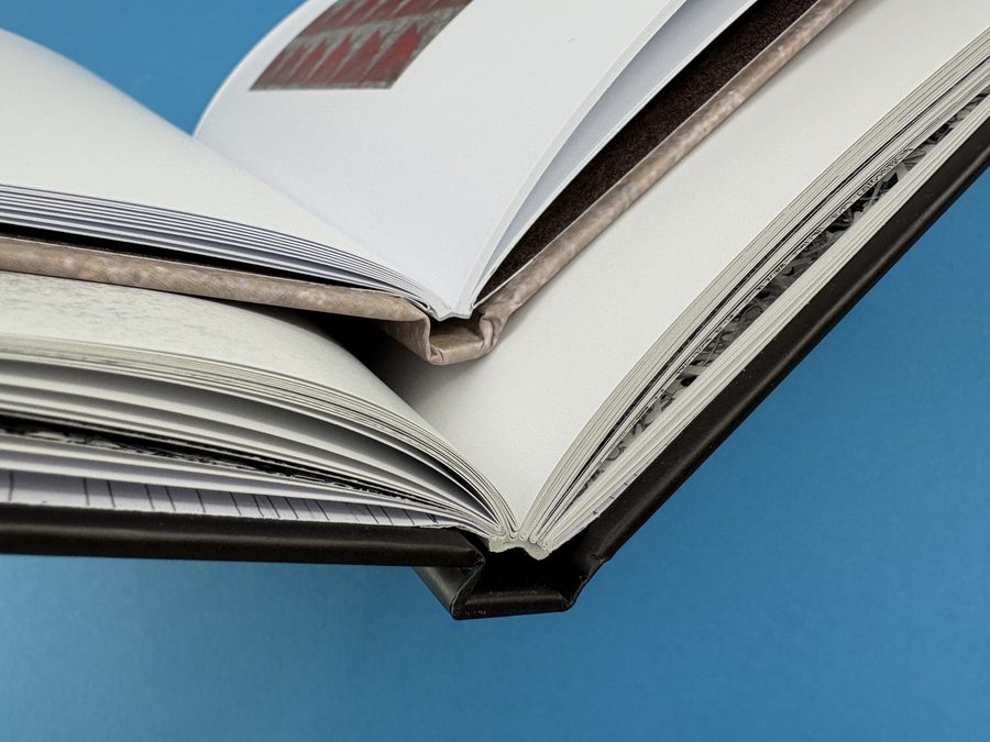 Two open hardback books compared close up: a glued spine above, and section sewn binding in folded sections below.