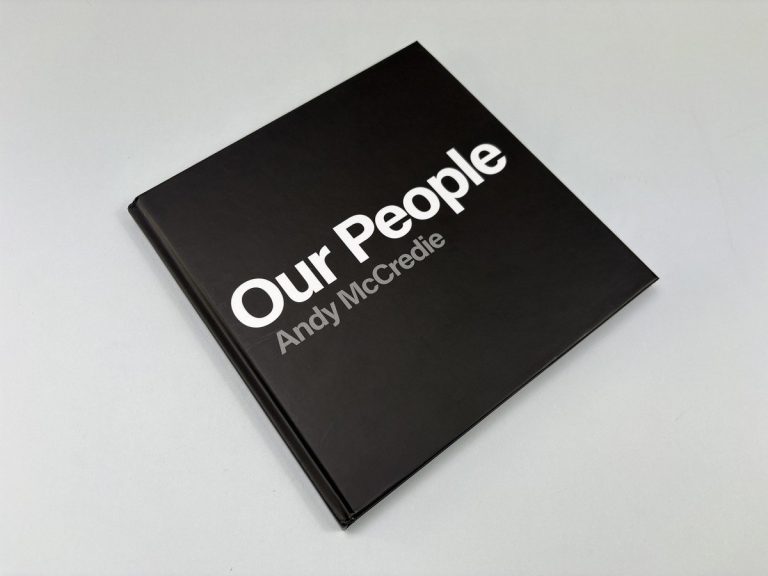 Black square hardback photobook cover with Our People and Andy McCredie in white type, matt laminated, on a pale backdrop.