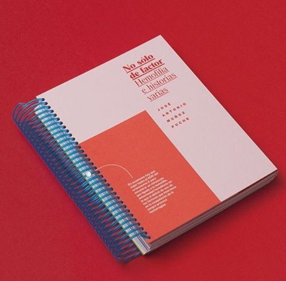 A spiral bound booklet with a pink cover lying on a red background.