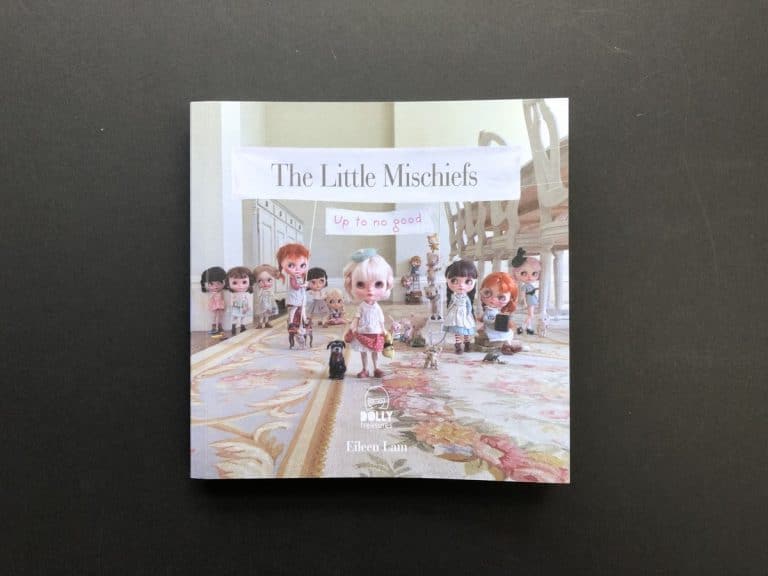 Square paperback cover of The Little Mischiefs, a row of big eyed dolls under a paper banner on a floral rug.